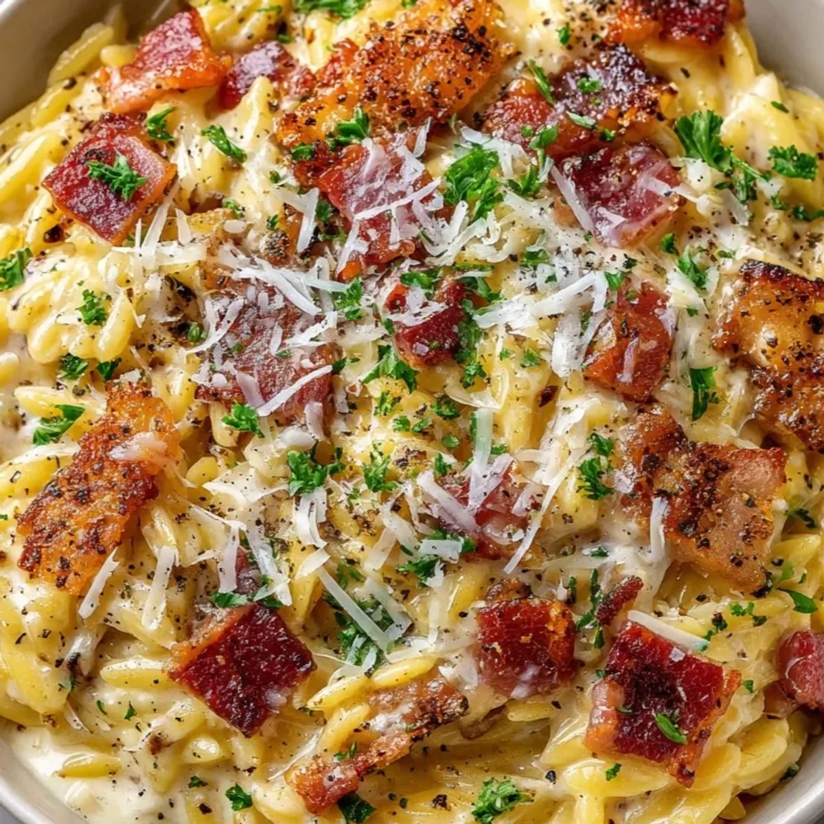 Close-up of creamy Orzo Carbonara Style, glistening with Parmesan and flecks of crispy pancetta.