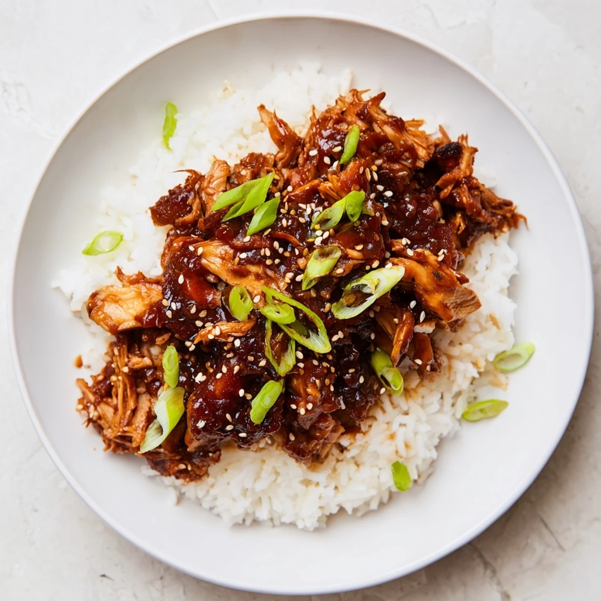 Tender, glistening Easy Slow Cooker Teriyaki Chicken atop fluffy rice, garnished with green onions and sesame seeds.