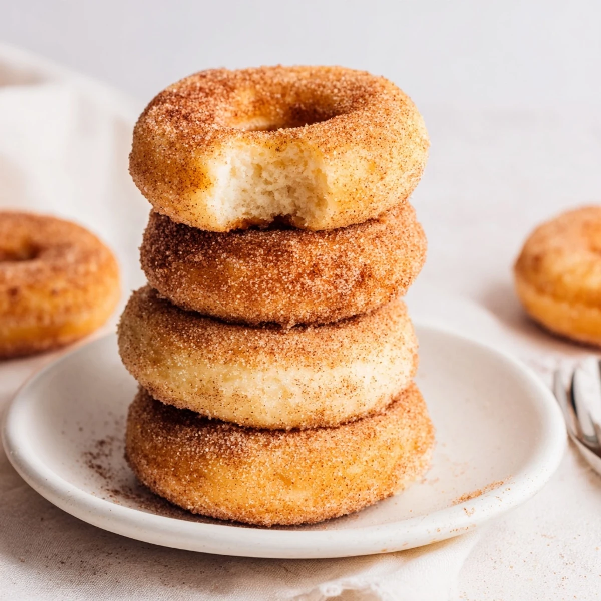 Perfectly round air fryer cinnamon sugar donuts, dusted in cinnamon sugar, next to a cup of coffee.