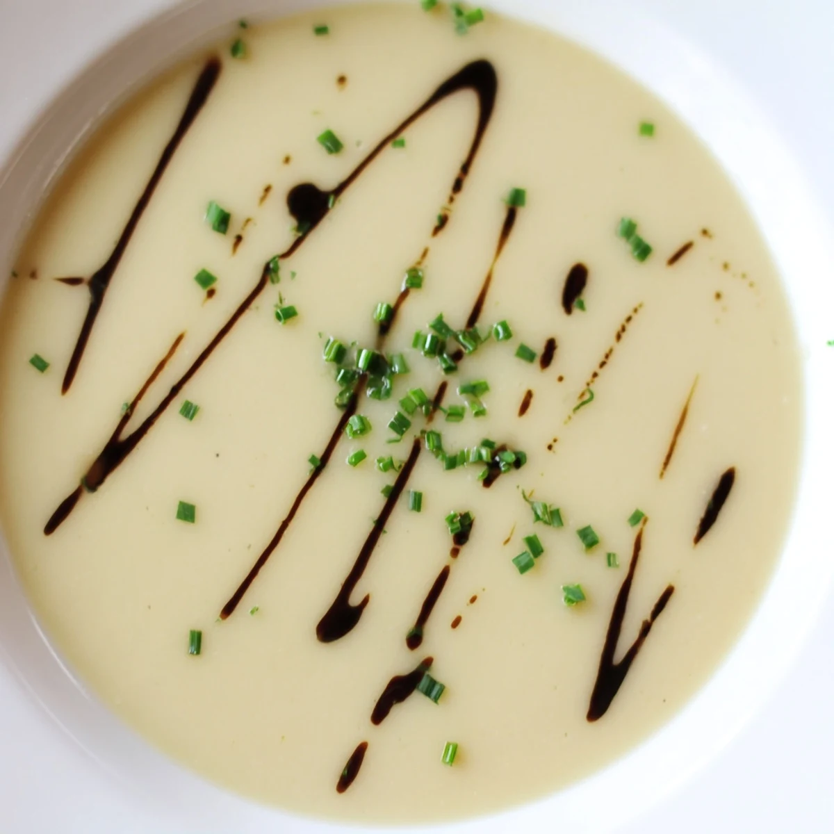 A bowl of creamy Celery Root Bisque garnished with fresh chives and a drizzle of cream, ready to serve.  
