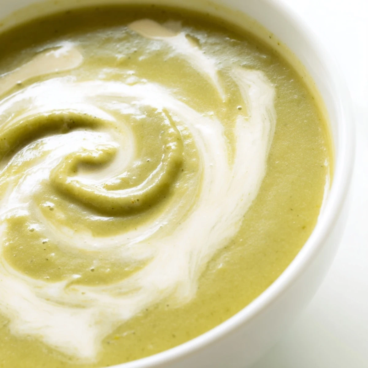 A close-up of creamy broccoli soup in a white bowl, topped with a swirl of cream and fresh chives, ready to enjoy.