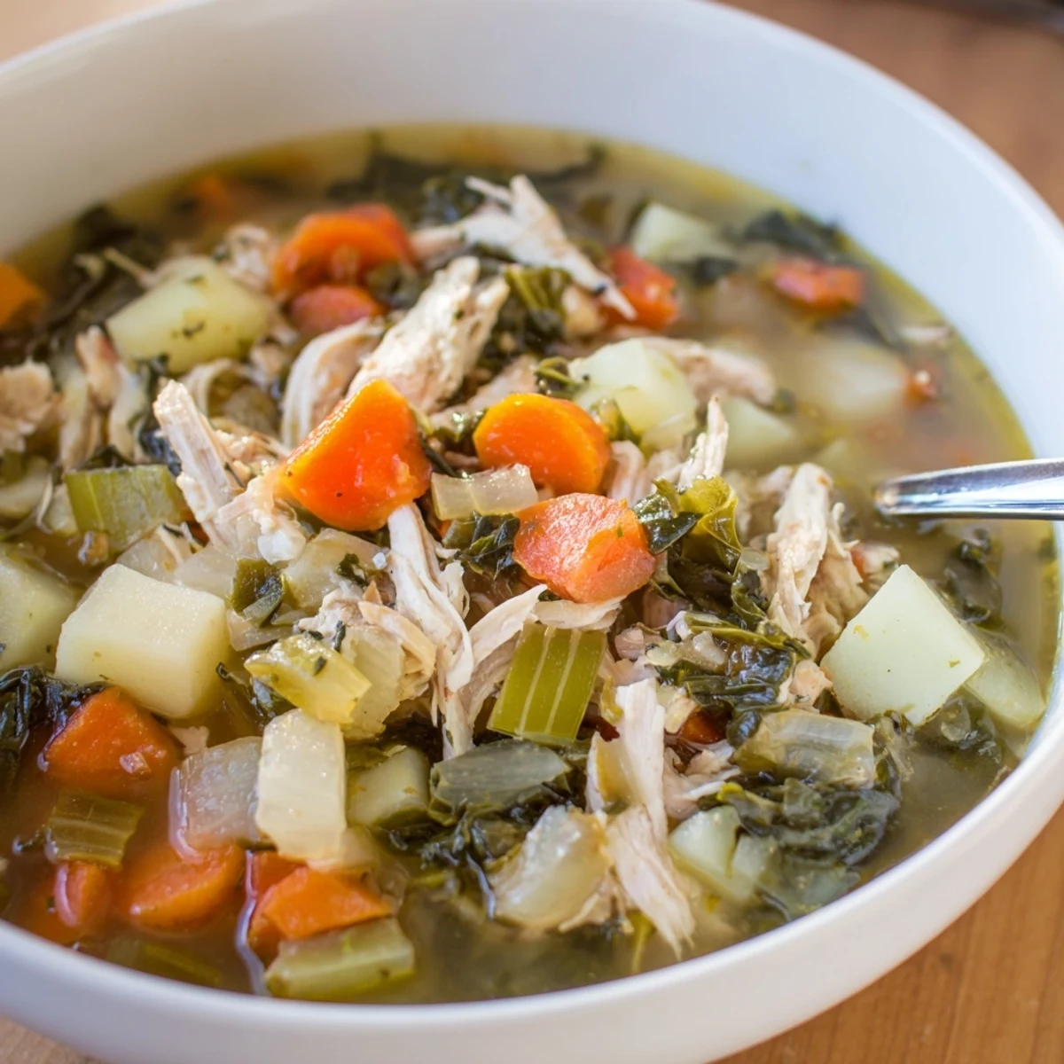 A steaming bowl of Collard Greens, Chicken and Vegetable Soup, featuring tender shredded chicken and potatoes in a clear, savory broth.