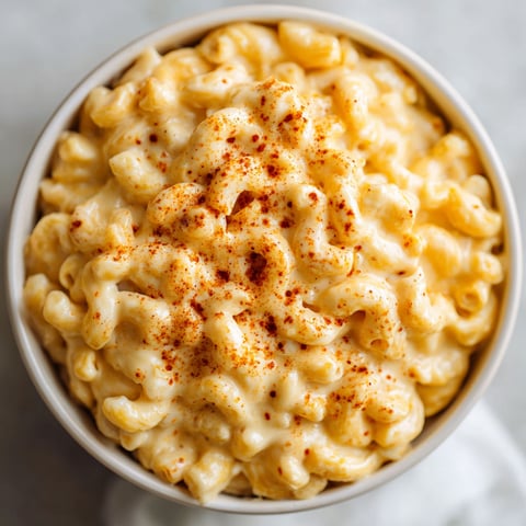 A bowl of macaroni and cheese with a sprinkle of red pepper on top.