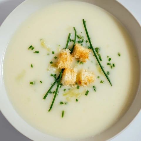A steaming bowl of creamy Potato Leek Soup, garnished with fresh, green herbs.