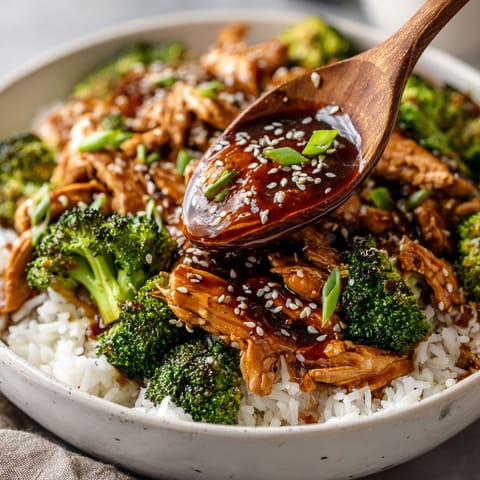 A bowl of chicken and broccoli with a wooden spoon.