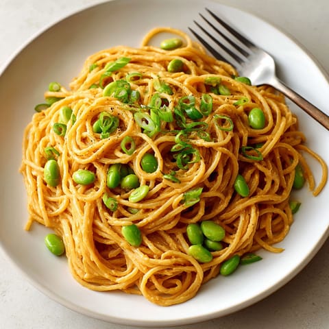 A plate of pasta with green peas and a fork.