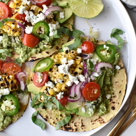 Delicious Sweet Corn & Basil Pesto Tacos garnished with feta and lime wedges.  