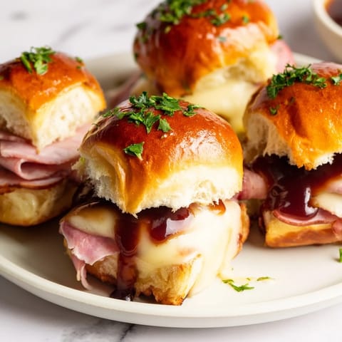 Melted Swiss cheese bubbles atop a cherry-glazed ham and cheese slider mashup, a sweet and savory delight.