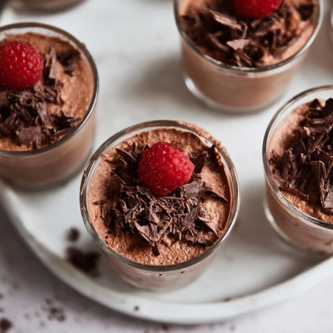 Delicate shot glasses filled with rich, creamy chocolate mousse dessert cups, garnished with berries.