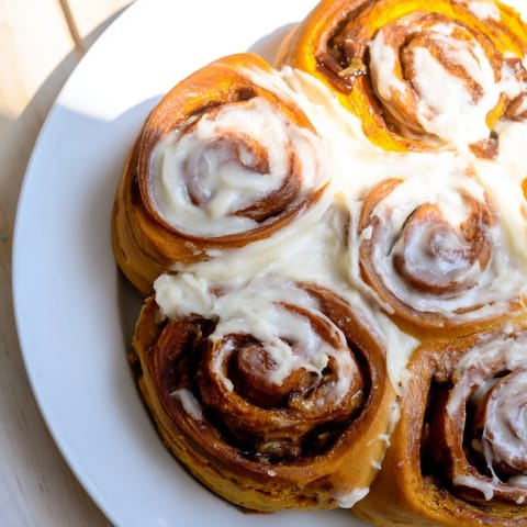 Warm and golden pumpkin cinnamon rolls, soft swirled dough, topped with cream cheese frosting, delicious.