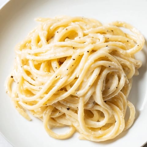Close-up of Cacio e Pepe, showcasing al dente spaghetti tossed in a peppery, cheesy sauce on a rustic plate.