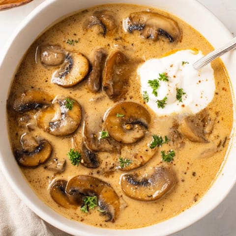 A hearty bowl of creamy mushroom stroganoff soup served with crusty bread on a wooden table.