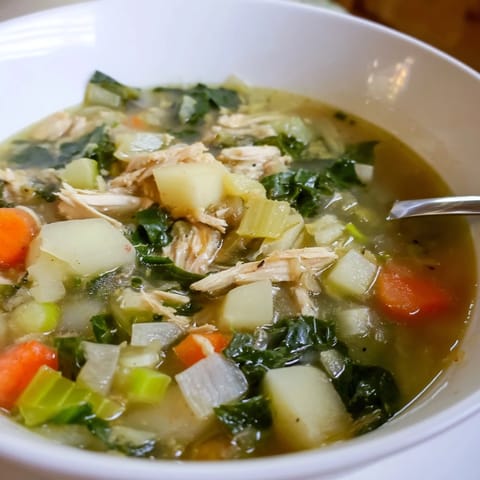 Close-up view of Collard Greens, Chicken and Vegetable Soup, highlighting vibrant green leaves and diced carrots floating in the hearty liquid.
