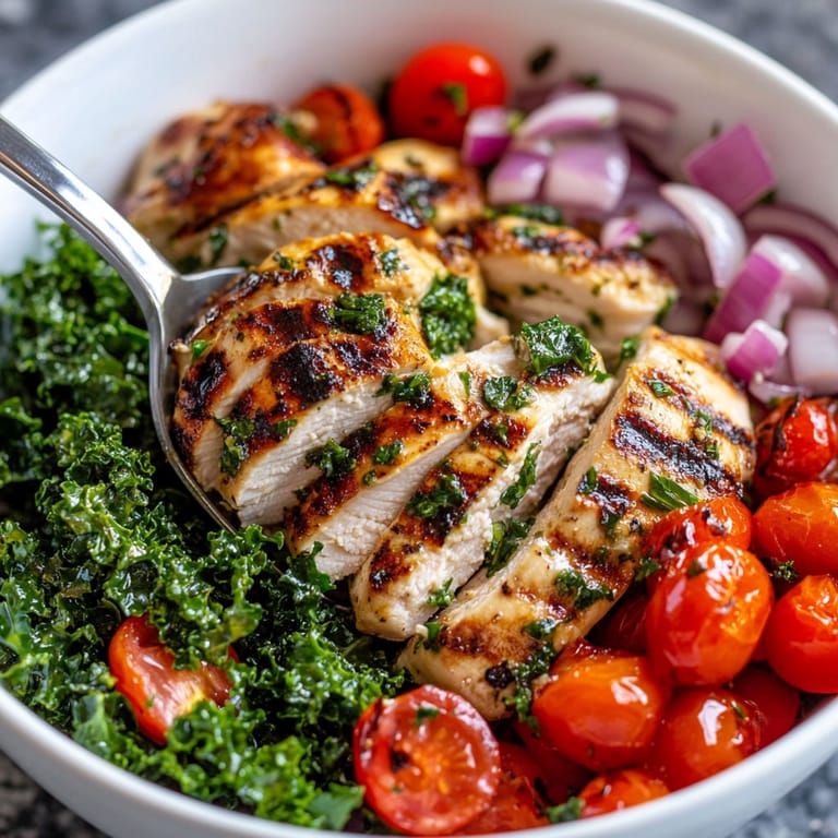 A bowl of food with chicken, tomatoes, onions, and kale.