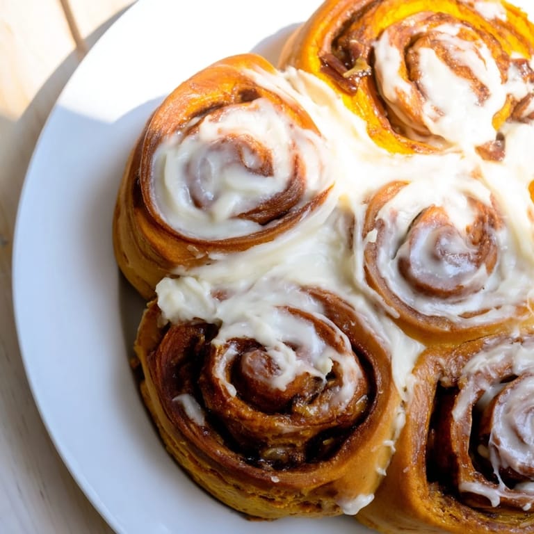 Warm and golden pumpkin cinnamon rolls, soft swirled dough, topped with cream cheese frosting, delicious.