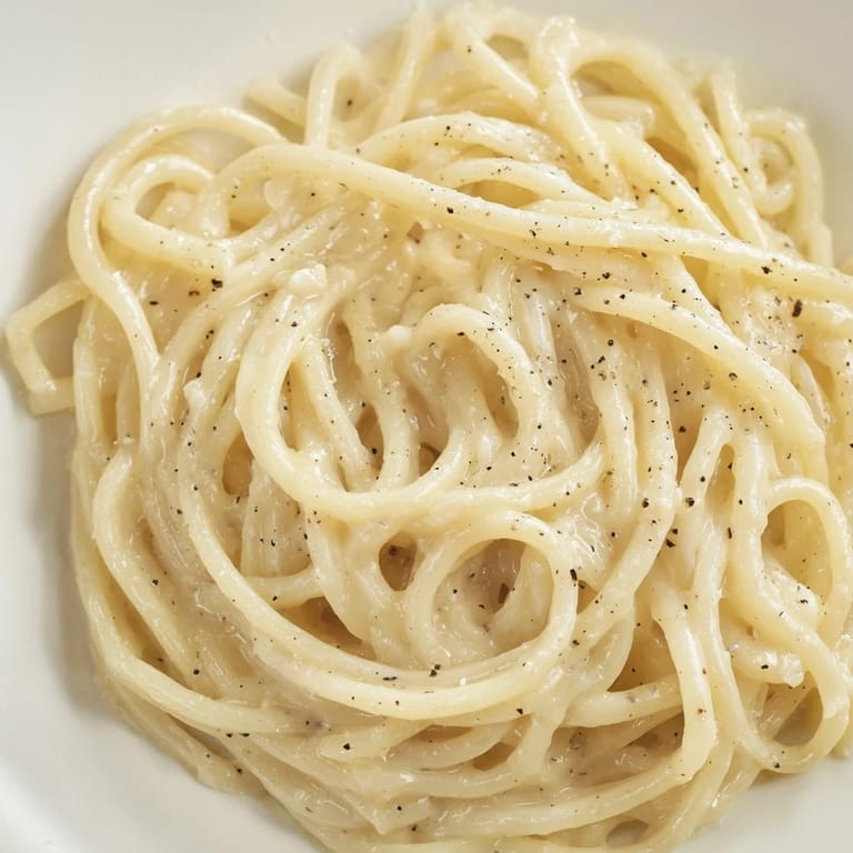 Freshly cracked black pepper sprinkled over a warm bowl of Cacio e Pepe, ready to be served for dinner.