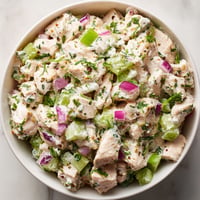A bowl of chicken salad with onions and herbs.